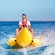 A man and a small child riding an inflatable watercraft shaped like a banana